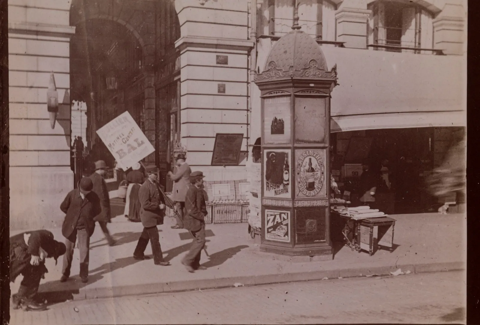 Un kiosque à journaux parisien au début du XXᵉ siècle, entouré de passants.